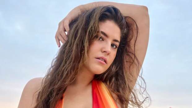 Gigi Robinson poses in a red and orange bikini with her arm over her head.